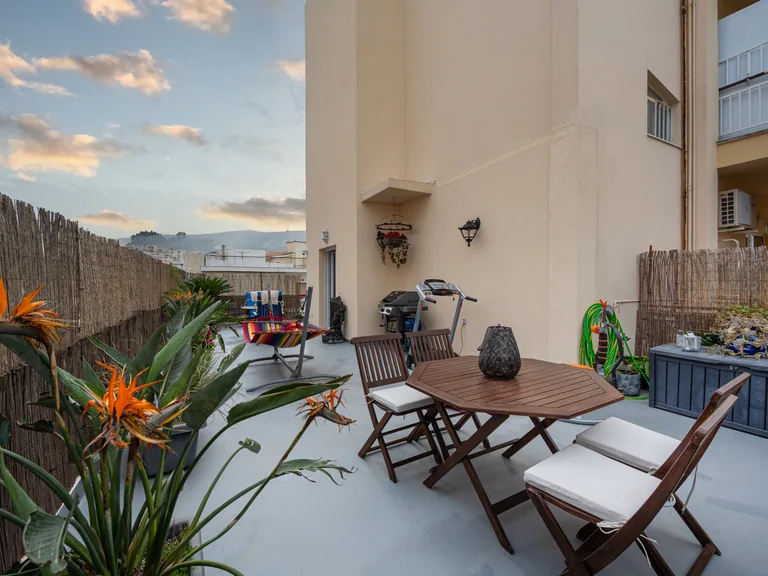 Spacious furnished terrace with wooden seating, plants and an open evening sky.