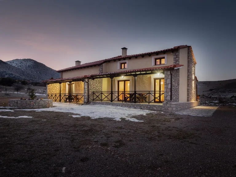 Chalet Renata 1 exterior at dusk with warm interior lights and the Parnassos mountains beyond.