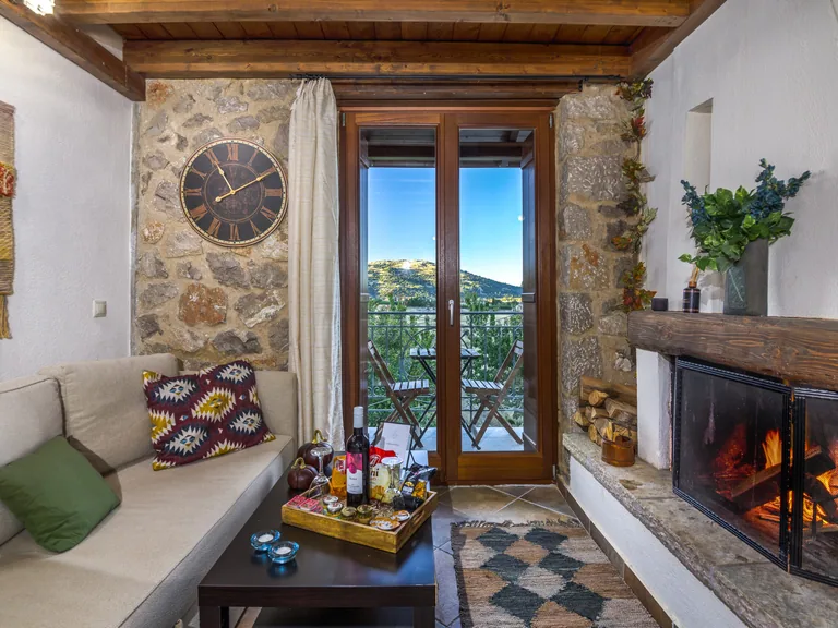 Stone-walled living area with a lit fireplace, sofa and balcony doors.