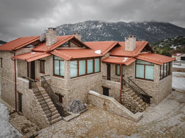 Stone residence with red-tiled roofs against a snow-dusted mountain backdrop.