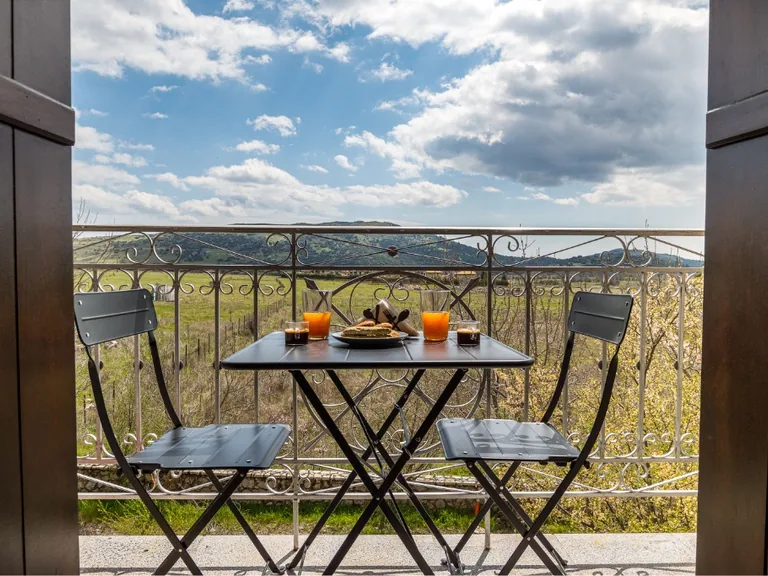 Balcony table and chairs overlooking green hills and distant mountains.