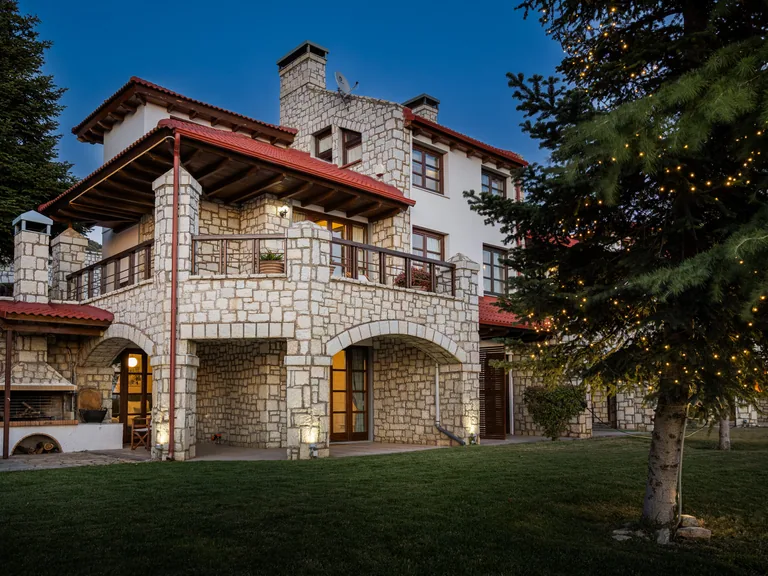 Stone-built property with timber balconies, arched openings and a green lawn at dusk.